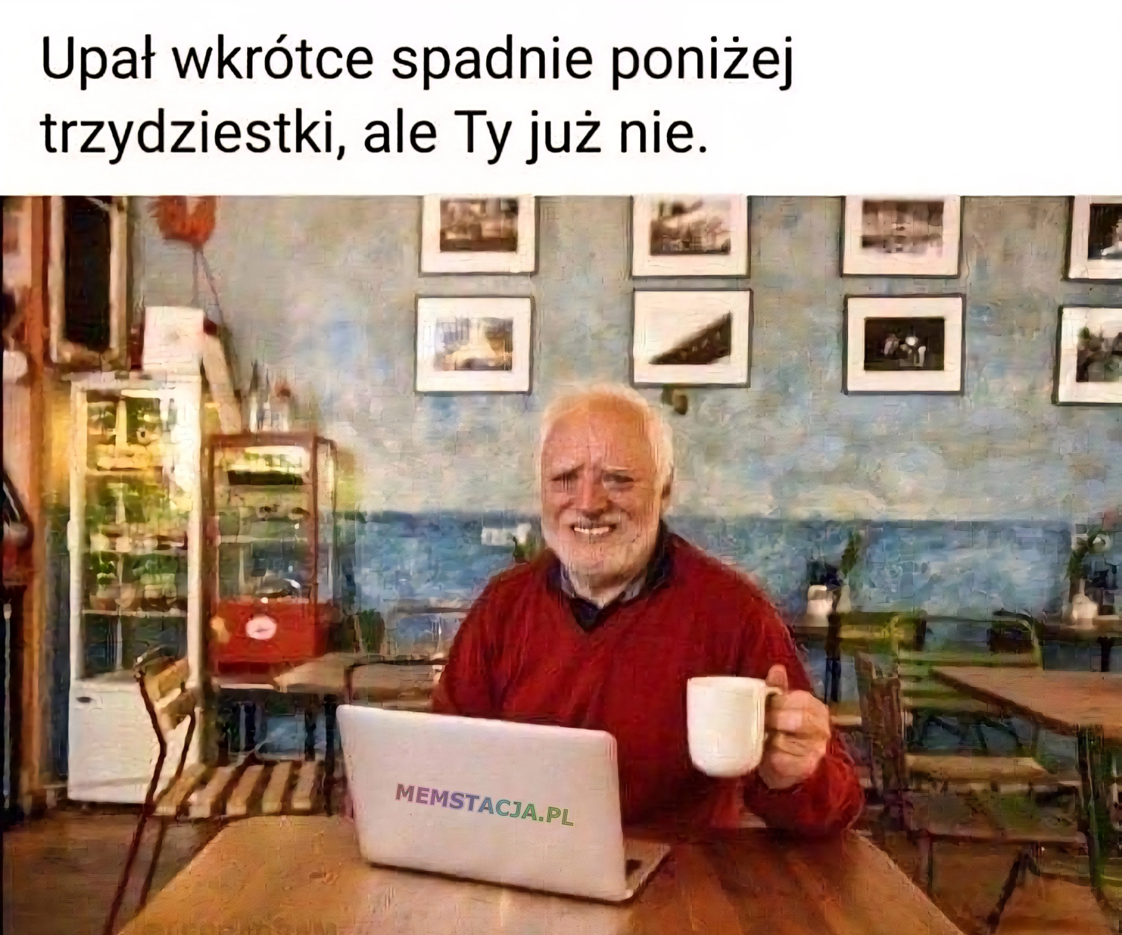 Mężczyzna z siwą brodą w czerwonym swetrze, trzymający kubek i siedzący przy laptopie – humorystyczny mem o starzeniu się.